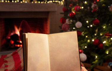 Christmas relaxation at home. Man holding an open blank pages book, burning fireplace background.