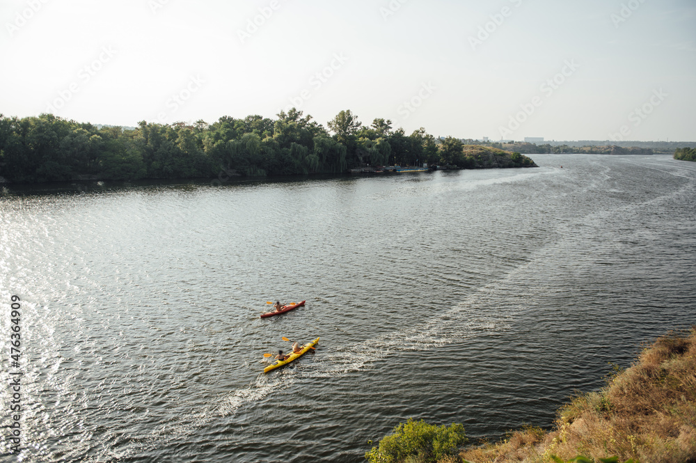 Fototapeta premium Two women and one man kayaking in the river at summer morning. Back view