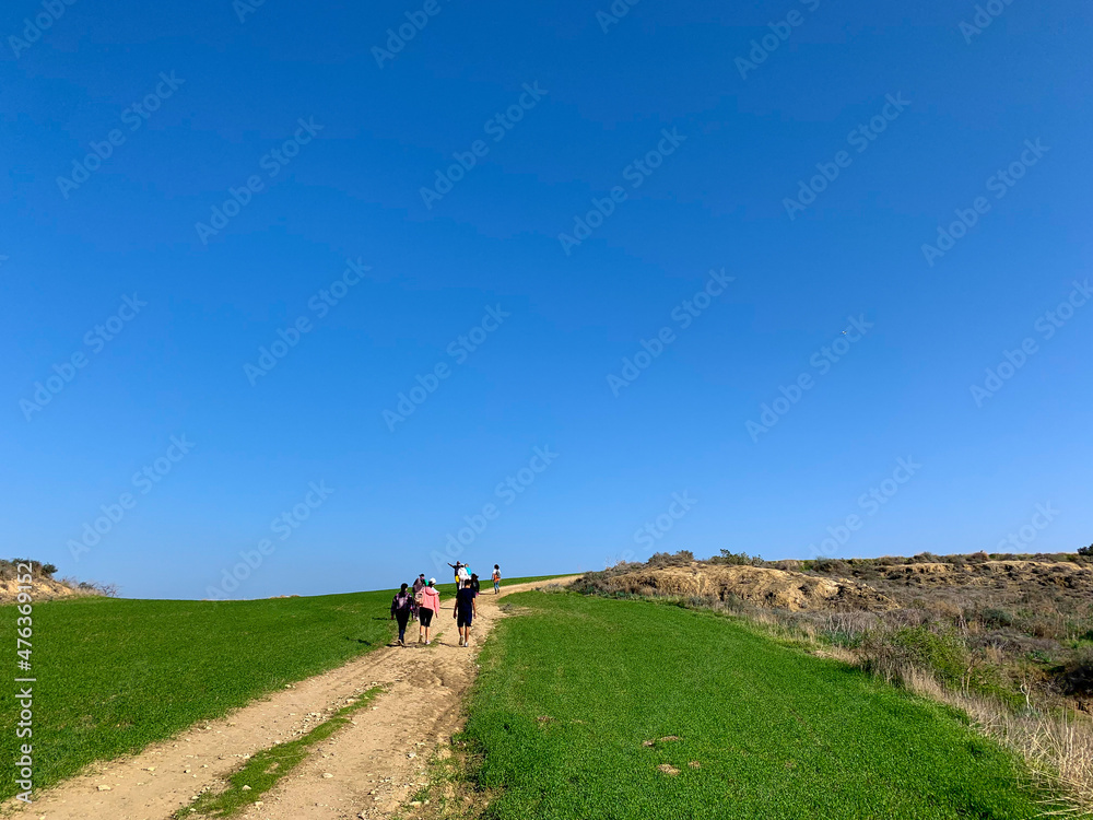 People silhouettes walking on the green field, blue sky, green grass, idyllic