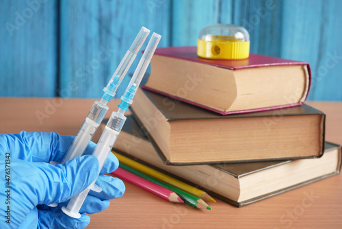 bottles and syringes of vaccine aganist covid-19 near book pile and school supplies, children vaccination concept photo