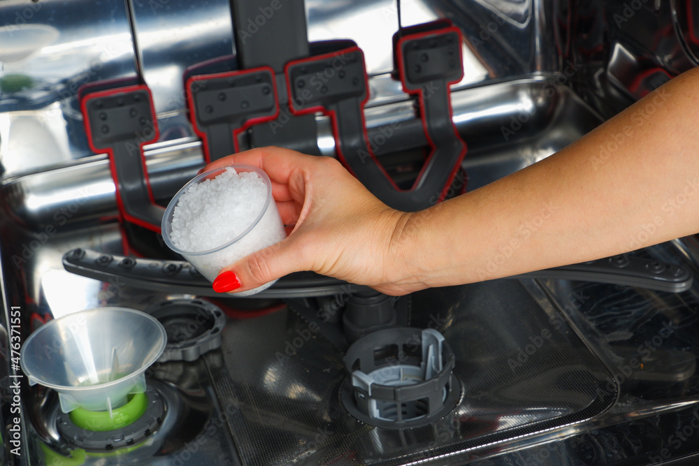 Adding salt to the dishwasher. A woman's hand pours salt to soften the