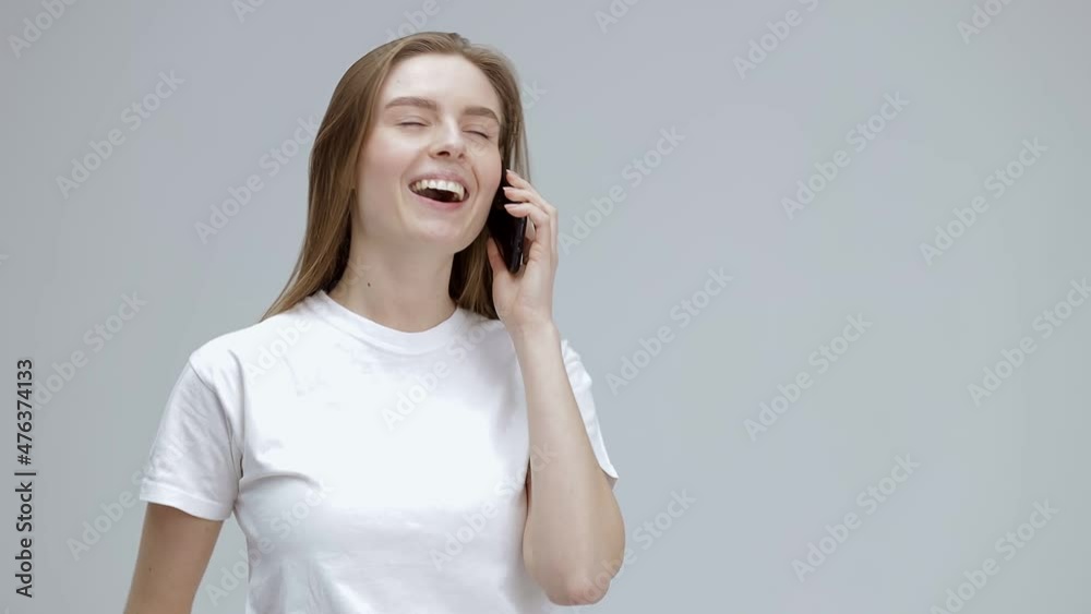 Excited young woman answering the phone, standing isolated on gray studio background, happy young woman enjoying pleasant conversation with friend, holding smartphone, talking. Happiness emotion Excited young woman answering the phone, standing isolated on gray studio background, happy young woman enjoying pleasant conversation with friend, holding smartphone, talking. Happiness emotion
