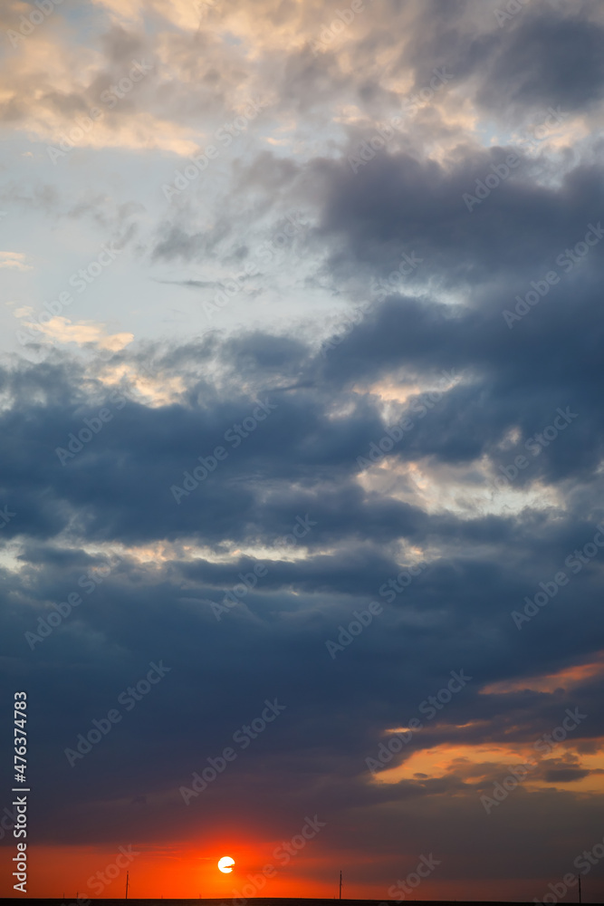 the setting sun in red against a background of blue clouds and a sky of blue, gold and white
