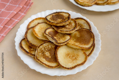 Heap of fried pancakes in white plate on beige background