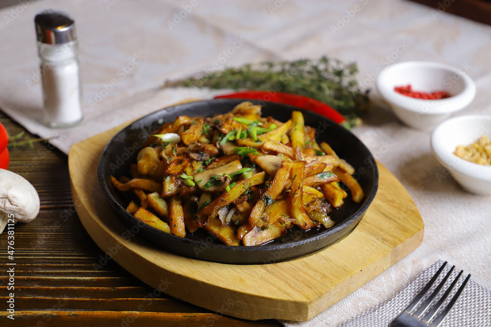 In a frying pan, fried potatoes are served on a wooden light stand, cutlery, hot red peppers, spices, white champignon. In a frying pan, fried potatoes are served on a wooden light stand, cutlery, hot red peppers, spices, white champignon.