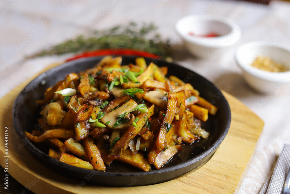 In a frying pan, fried potatoes are served on a wooden light stand, cutlery, hot red peppers, spices, white champignon. In a frying pan, fried potatoes are served on a wooden light stand, cutlery, hot red peppers, spices, white champignon.