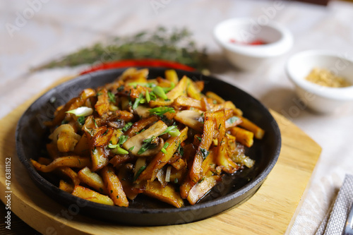 In a frying pan, fried potatoes are served on a wooden light stand, cutlery, hot red peppers, spices, white champignon.