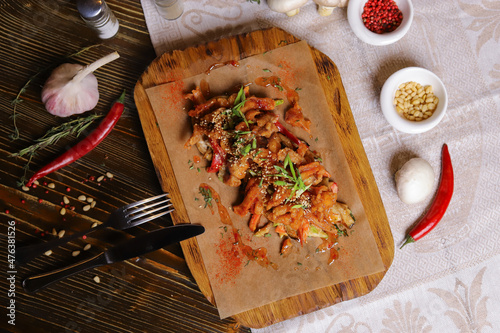 On a dark countertop, a light linen napkin, on a cutting board Seafood Squid in batter with sauce and spices on a board on a dark table top, cutlery, a head of garlic, white champignon