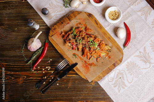 On a dark countertop, a light linen napkin, on a cutting board Seafood Squid in batter with sauce and spices on a board on a dark table top, cutlery, a head of garlic, white champignon