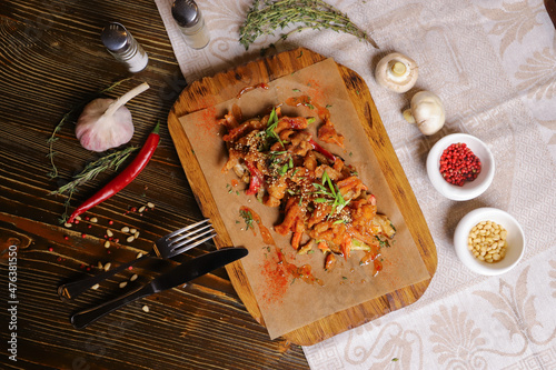 On a dark countertop, a light linen napkin, on a cutting board Seafood Squid in batter with sauce and spices on a board on a dark table top, cutlery, a head of garlic, white champignon