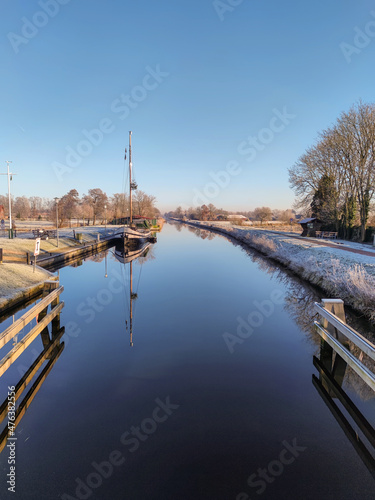Kanal im Winter mit einer glatten Wasseroberfläche und Frost auf dem Deich © vsnyder