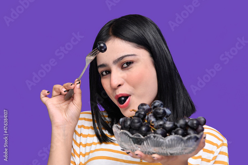 foodie girl holding bowl of grapes and grape her mouth indian pakistani modle photo