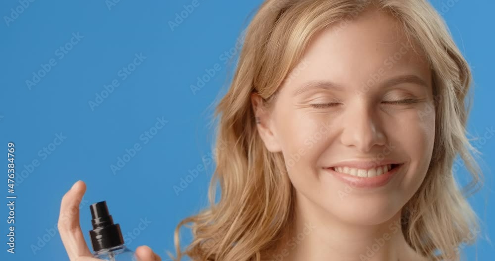 Blonde woman sprays micellar water to her face. Women's cosmetics usage. Beauty care procedures on blue screen, 4k Prores HQ