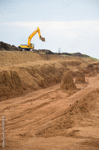 Yellow excavator works on the construction of roads, vertical