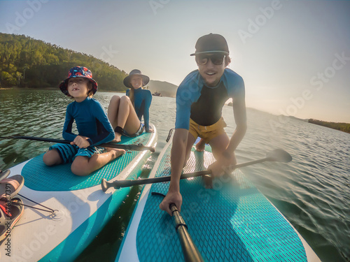 happy family of three, dad, mom and son, enjoying stand up paddling during summer vacation