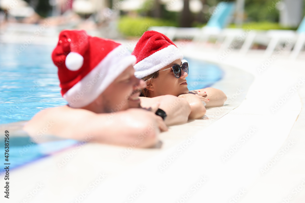Obraz premium A man and women in santaclaus hats are resting in the pool