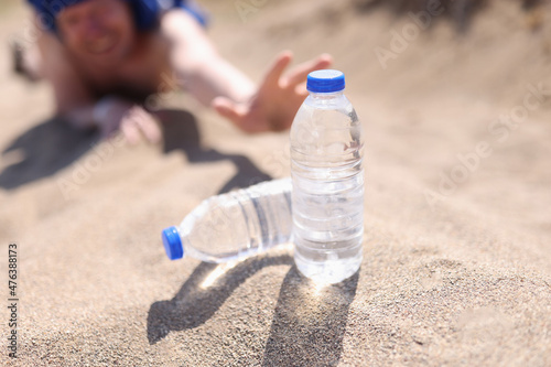 A man in the desert stretches on the sand for bottles of water