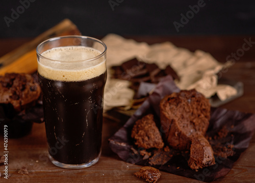 Glass of beer stout standing on wooden board next to chocolate muffin