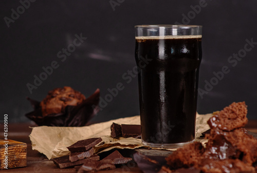 Photo Glass of beer stout standing on wooden board with chocolate muffin