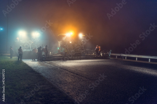 Laying asphalt paver at night with headlights. Road construction.