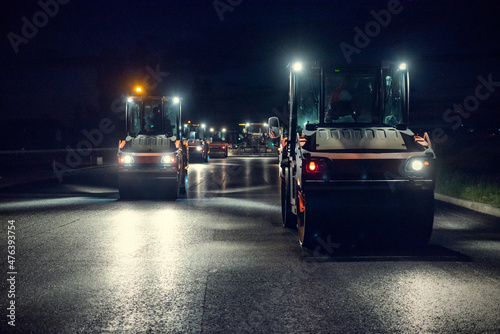 Rollers roll a layer of new asphalt at night by headlights © Andrii
