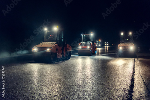 Rollers roll a layer of new asphalt at night by headlights © Andrii