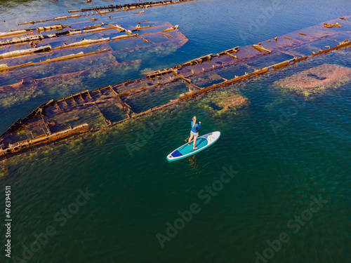 Woman on paddle board, sup next to Abandoned broken shipwreck sticking out of the sea