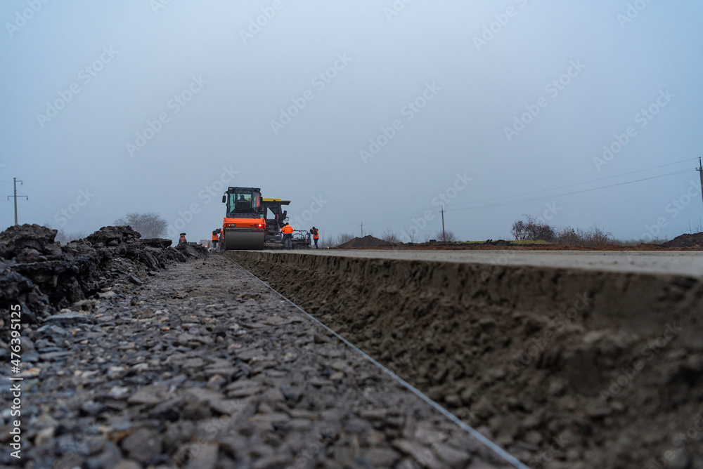 A roller compacts a layer of fresh concrete after a paver on a new road construction.