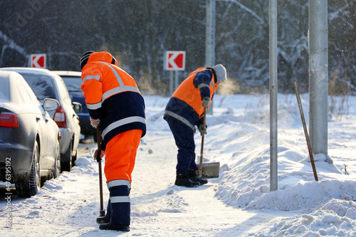 Fototapeta Naklejka Na Ścianę i Meble -  Snow removal in winter city at frost weather. Two men workers in uniform with a shovel and crowbar cleaning the street near the car  parking