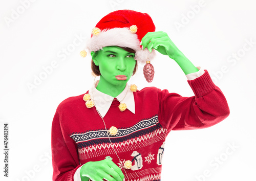 Image of a funny woman in a Christmas sweater posing on a white background with New Year's decorations. Grinch style. Holiday concept. photo