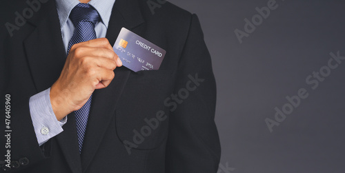 Businessman holding a blue credit card in a suit pocket while standing with gray background
