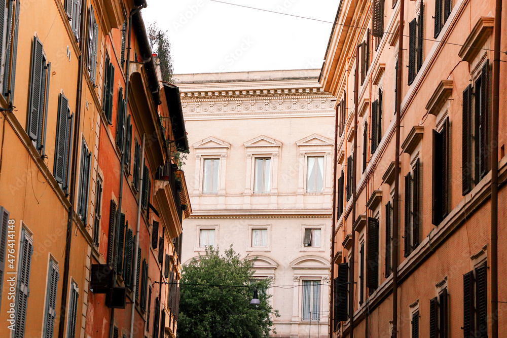 Road in Rome, Italy with orange and red buildings along the sides leading to a creme building at the end.