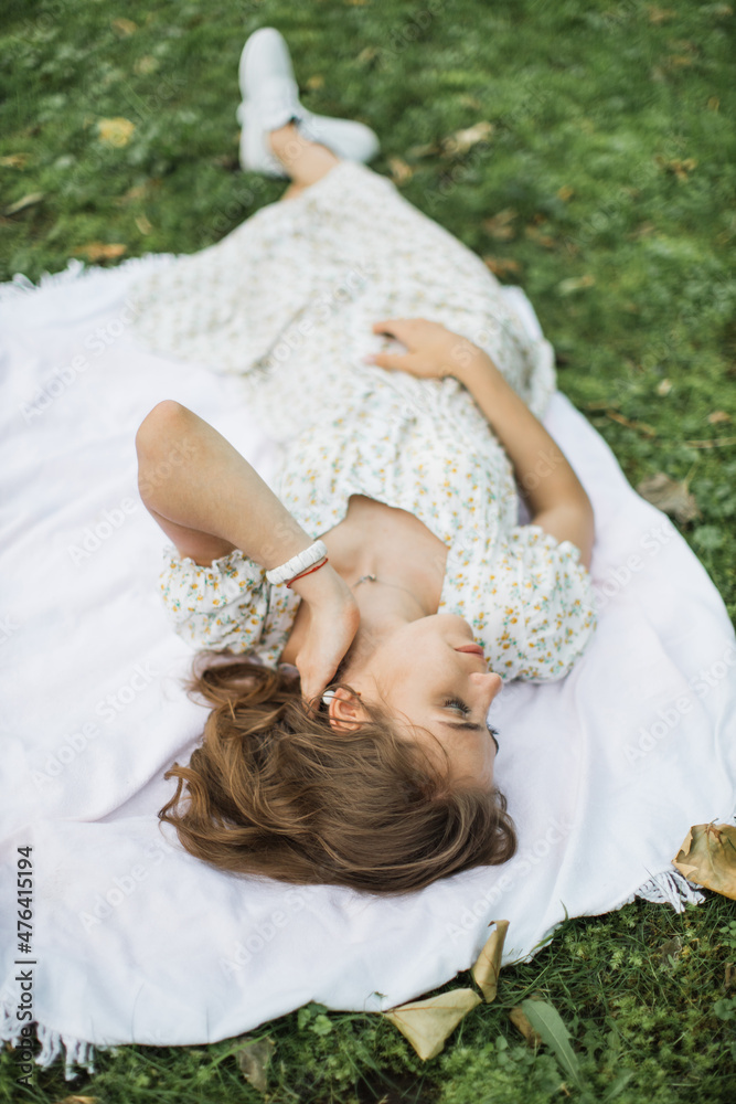 Fototapeta premium Portrait of young woman with physical disability in stylish summer dress smiling sincerely in camera at green park. Female person who lies on the green grass enjoying summer weather outdoors.