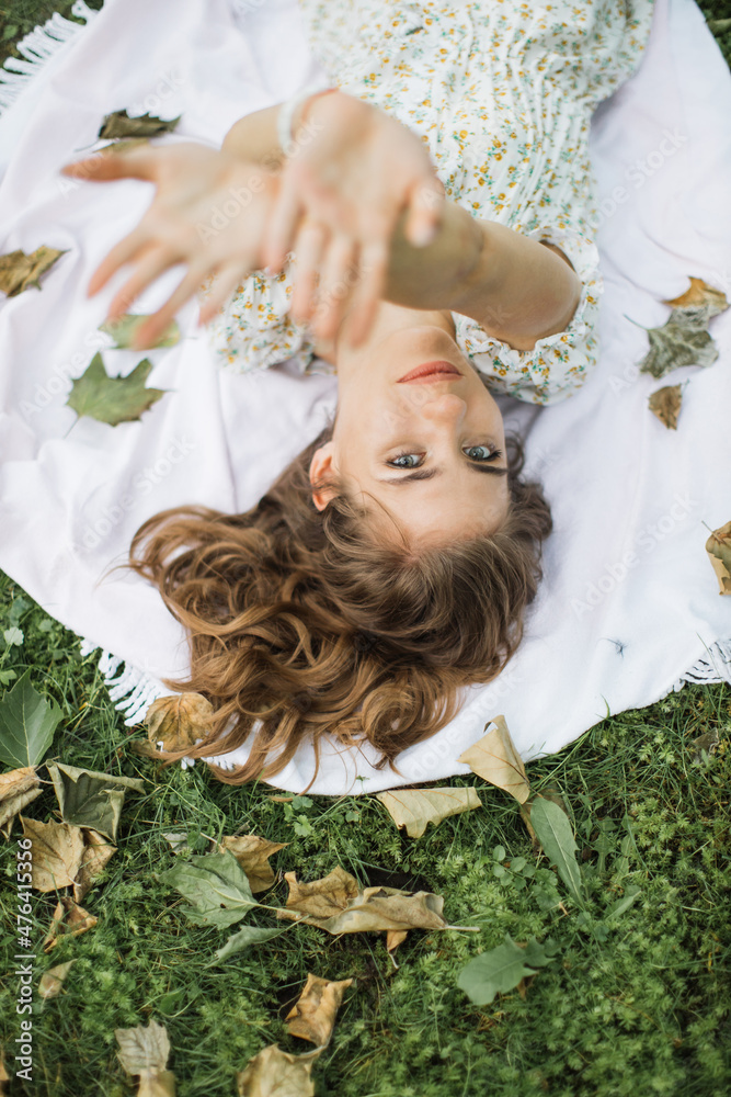 Naklejka premium Portrait of young woman with physical disability in stylish summer dress smiling sincerely in camera at green park. Female person who lies on the green grass enjoying summer weather outdoors.