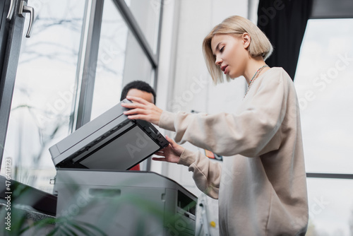 blonde woman using printer near african american manager.