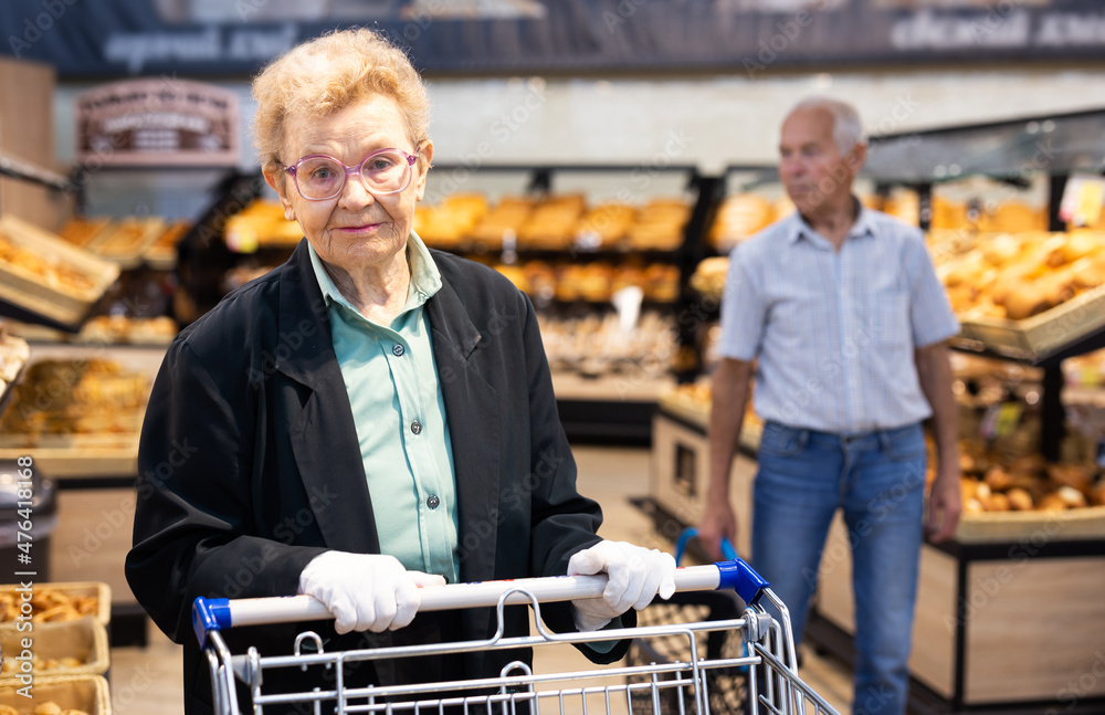 an elderly woman with glasses is shopping in the bread department of a supermarket
