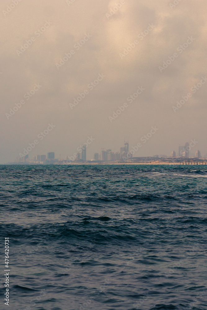 Landscape photo of a cityscape beyond the sea shore. At the front is the blue ocean on a gloomy day. Landscape photo of a cityscape beyond the sea shore. At the front is the blue ocean on a gloomy day.