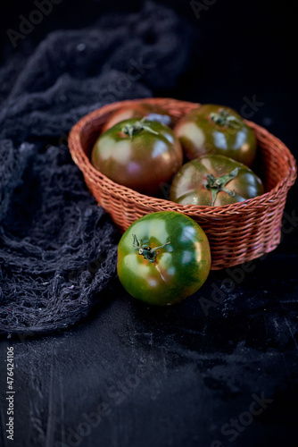 Green tomatoes in the basket on a dark background.. Black background for copying text. Restaurant business and advertising.