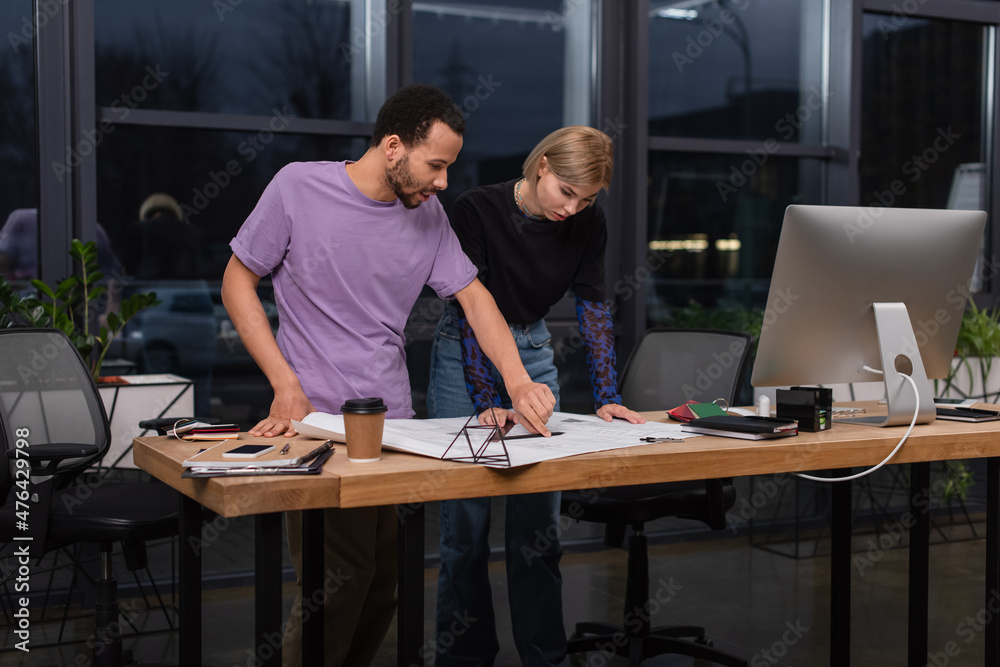 young interracial colleagues looking at blueprint on desk. young interracial colleagues looking at blueprint on desk.