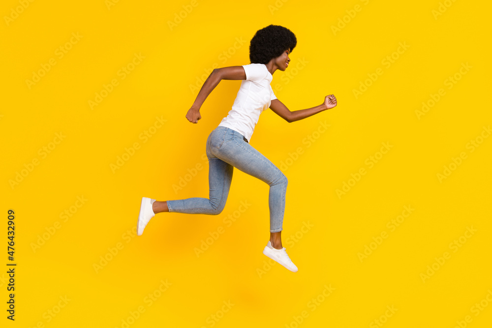 Full length photo of cute adorable dark skin woman dressed white t-shirt smiling running jumping isolated yellow color background