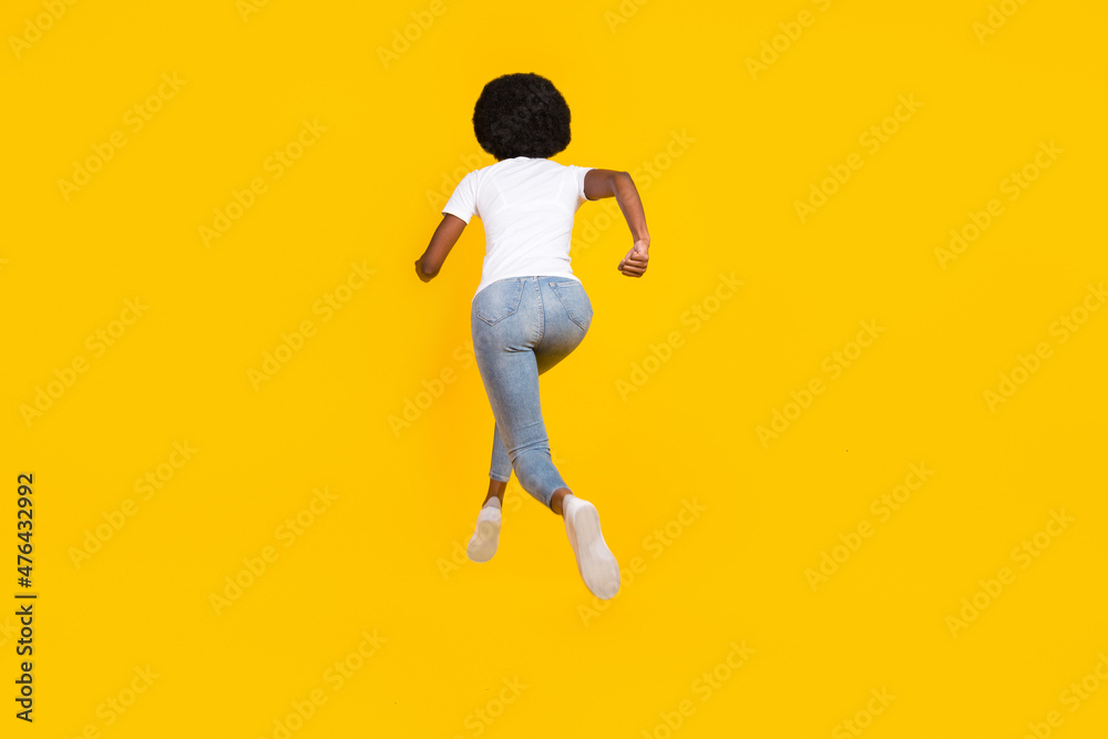 Full length photo of adorable shiny dark skin woman dressed white t-shirt running fast jumping isolated yellow color background