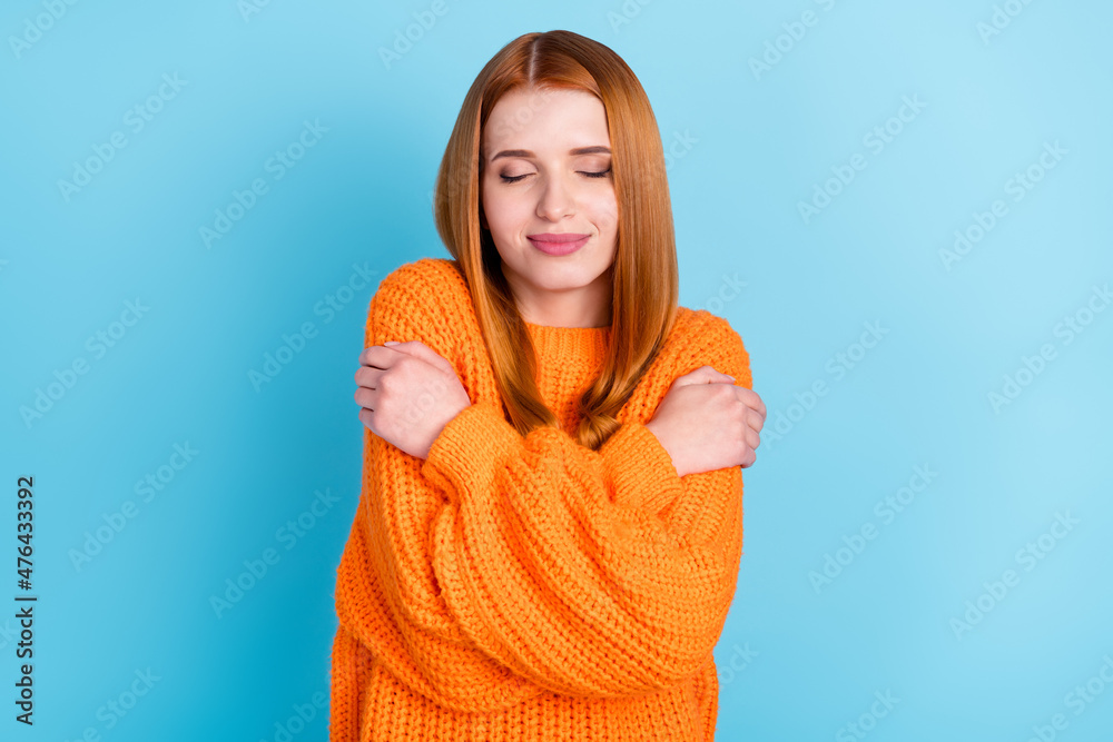 Photo of sweet red hairdo millennial lady hug herself wear orange sweater isolated on blue color background Photo of sweet red hairdo millennial lady hug herself wear orange sweater isolated on blue color background