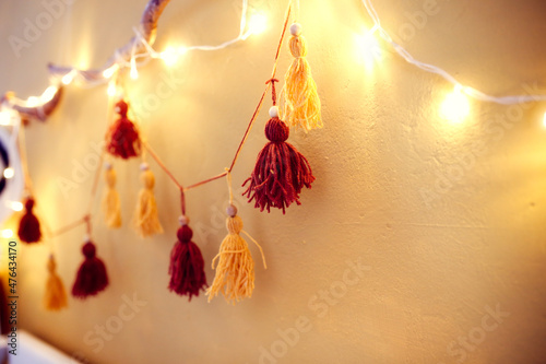 Fototapeta Naklejka Na Ścianę i Meble -  Cozy homemade garland from pompons from threads on the wall in the room, home decor Scandinavian style, mustard and brown, recycling