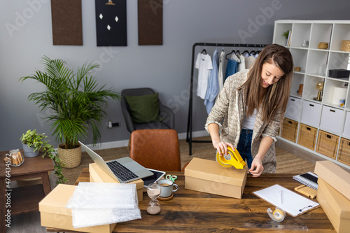 Young woman selling products online and packaging goods for shipping. Women, owener of small business packing product in boxes, preparing it for delivery. photo