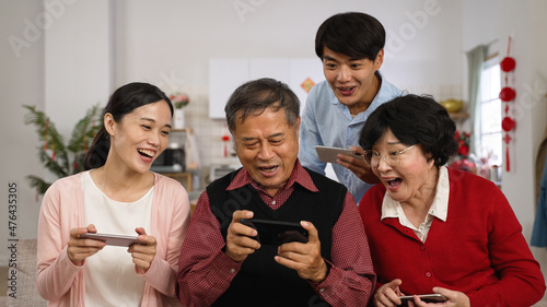 family members having fun playing games on smartphone during Chinese new year holiday at home. everyone leaning close to happy old father who just win the game