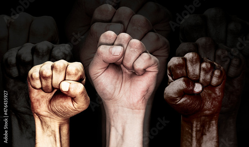 Hands of people of different nationalities and skin colors clenched into fists on a black background with reflection. The concept of combating racism, tolerance and emigration.