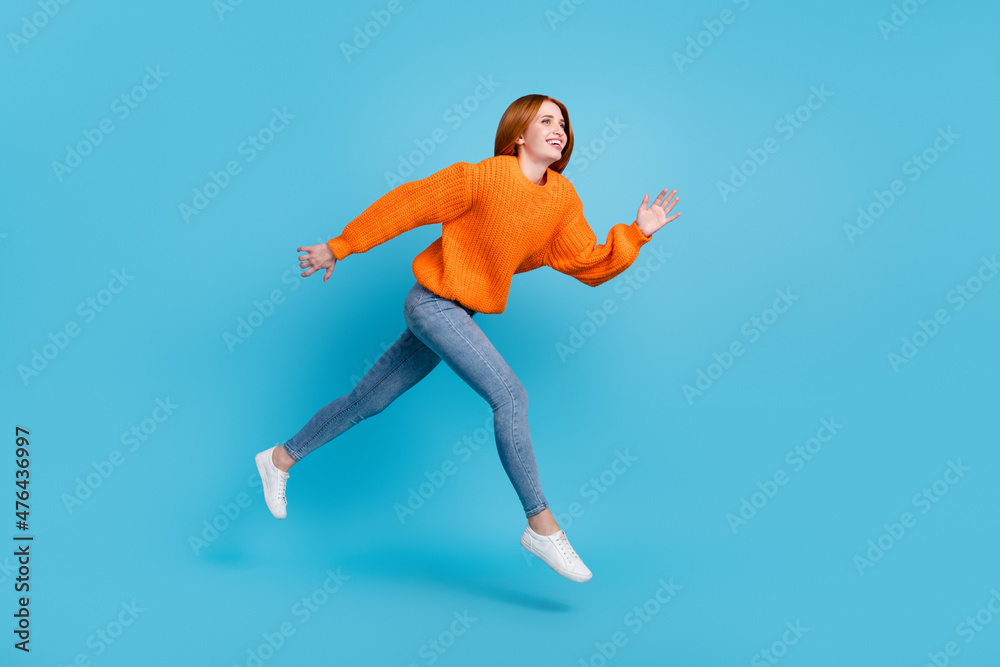 Photo of sweet adorable young woman wear orange sweater jumping high running fast smiling isolated blue color background