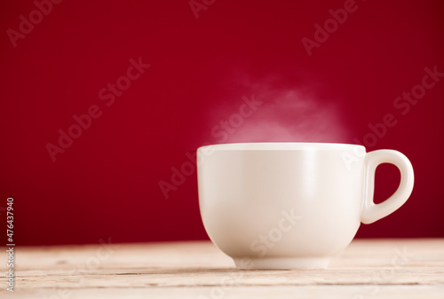 broken white cup of tea or coffee with hot steam smoke on rustic wooden table, red background