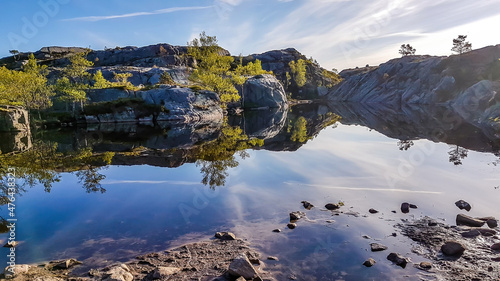 A shallow lake, located on the way to Preikestolen, Norway. Soft reflection of the mountains in the lake. Clear day. Slopes of the mountains surrounding the lake are overgrown with green plant.