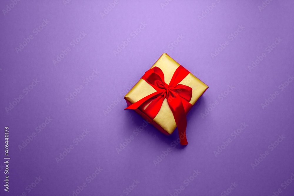 Holiday gift. Box in a gold gift wrapping with a red bow, on a pantone background. Merry Christmas Valentine's Day greetings. Postcard with love. High quality photo